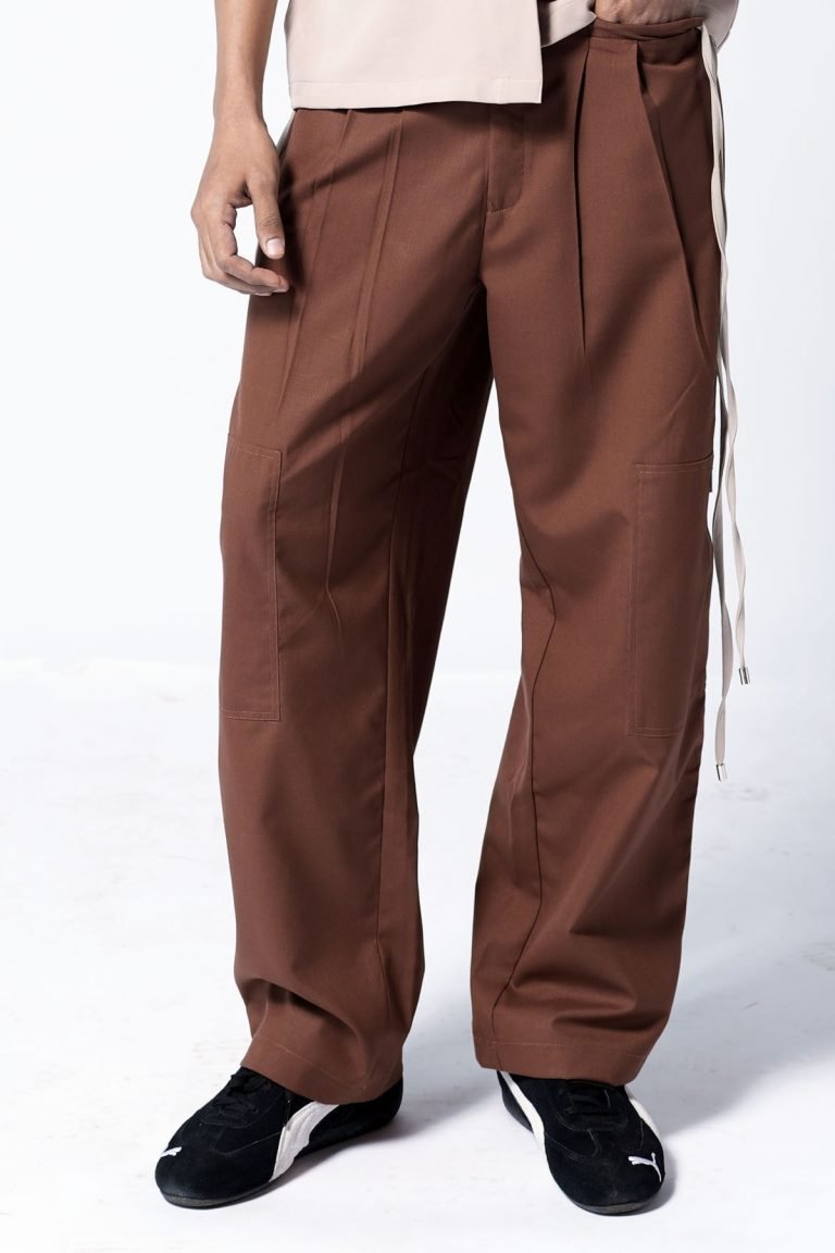 A person wearing brown, wide-legged brown parachute pants with pleats and black sneakers