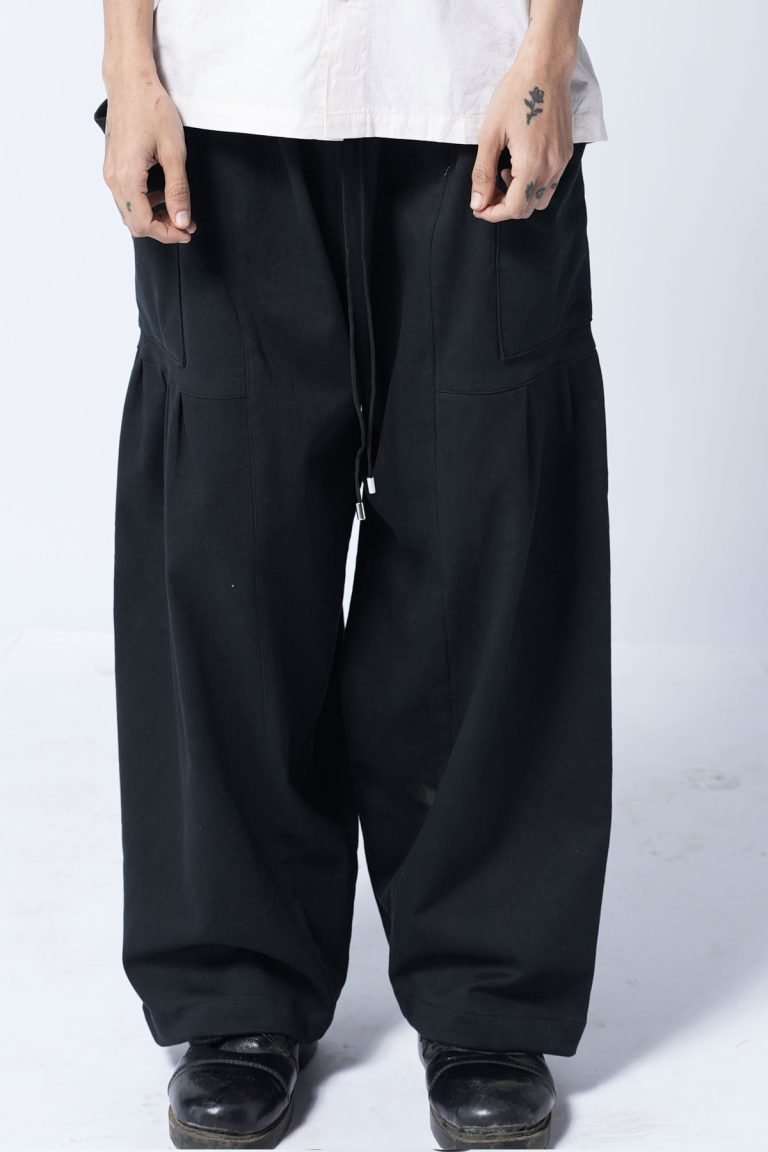 Man wearing wide black baggy pants with drawstring waist, standing against a plain background.