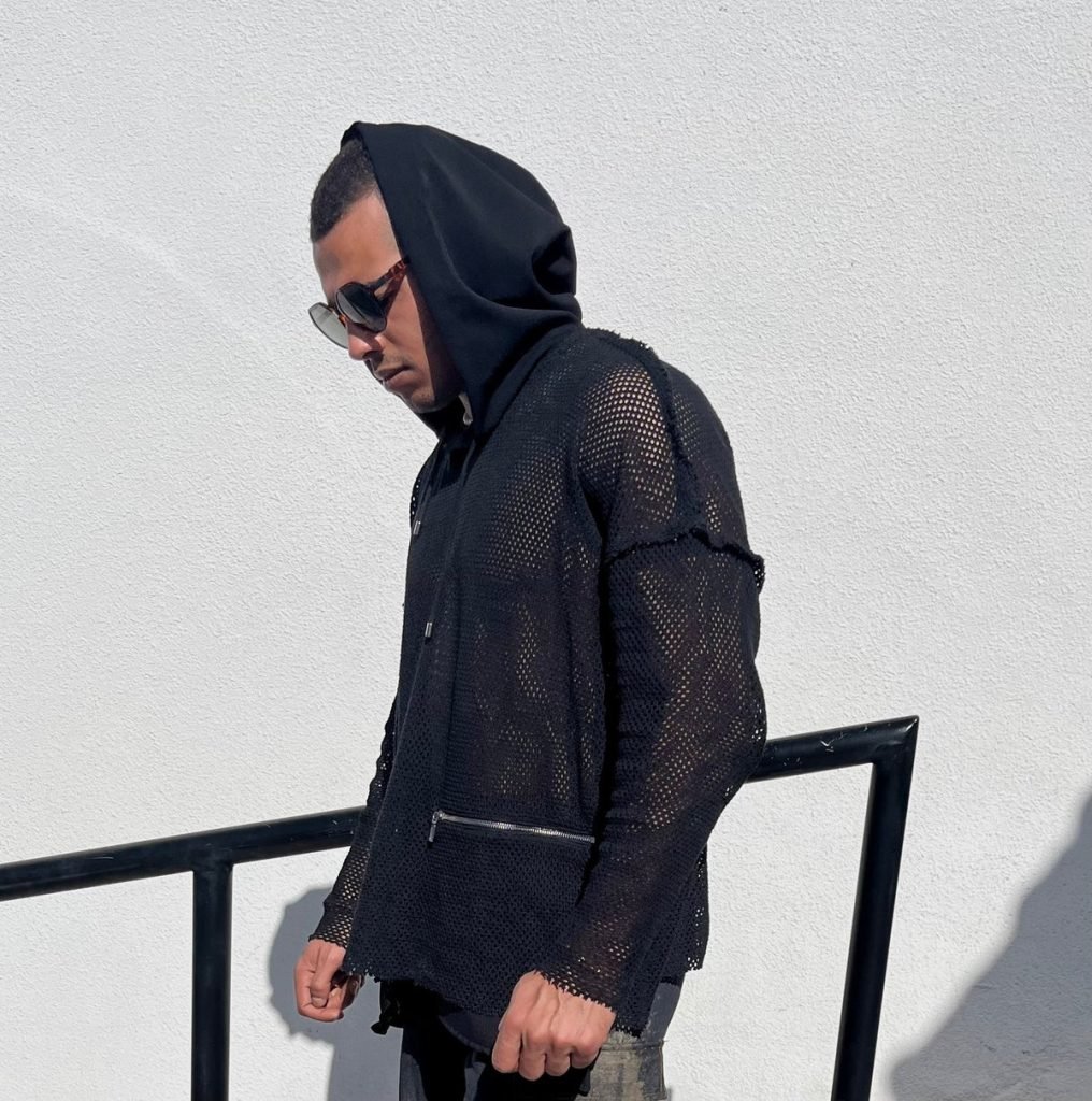 A man in a draft black hoodie and sunglasses, looking cool and casual.
